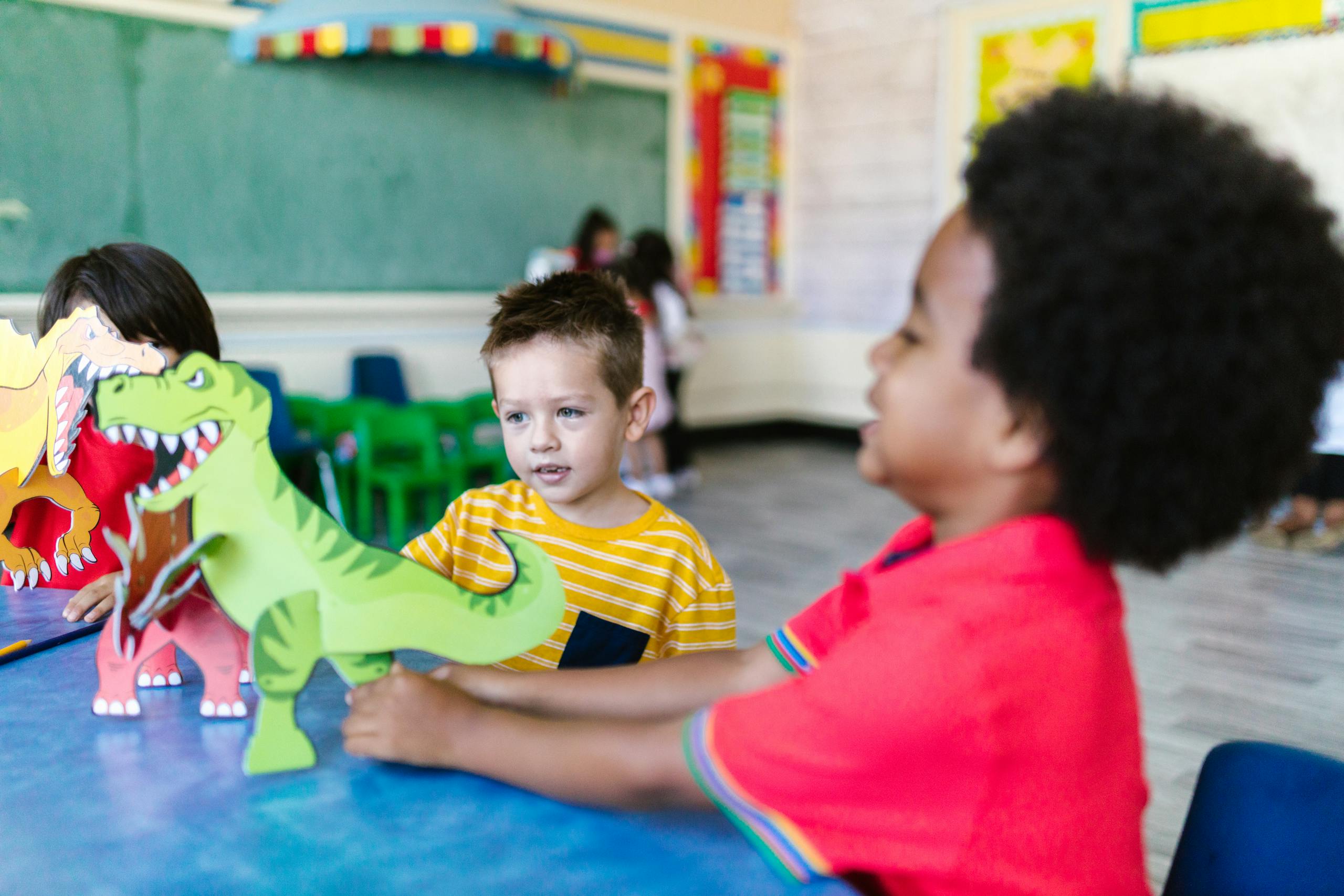 Kids enjoying playtime with dinosaur cutouts in a vibrant classroom setting.