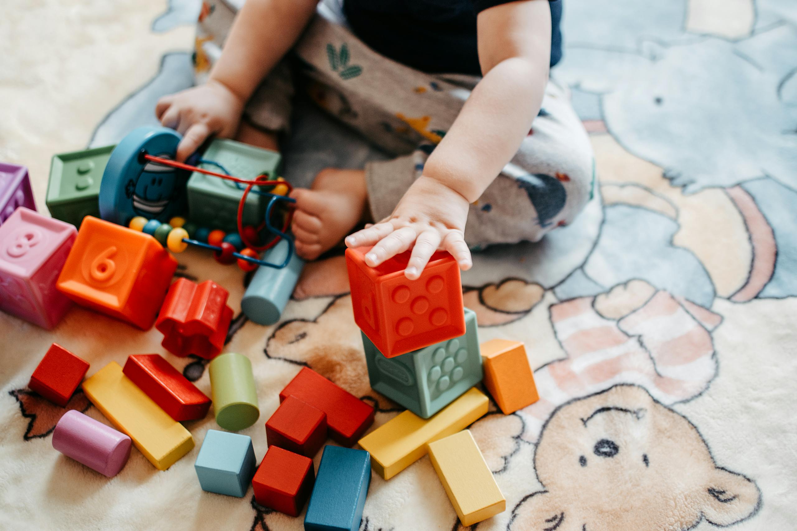 Toddler engaging with vibrant toy blocks on a patterned rug in a playful setting.